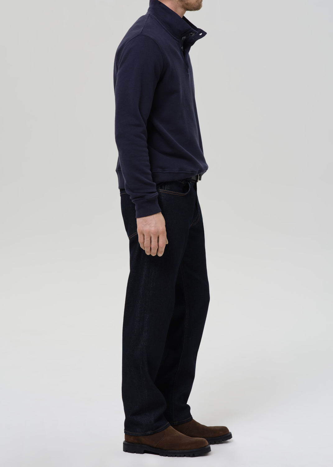 Person wearing a navy blue jacket and dark pants on a grey background