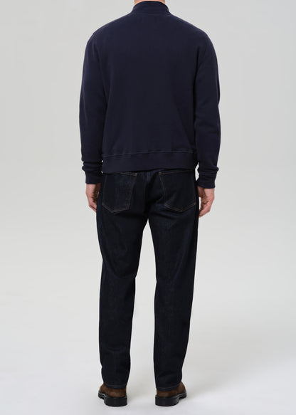 Person wearing a navy sweater and dark pants on a grey background