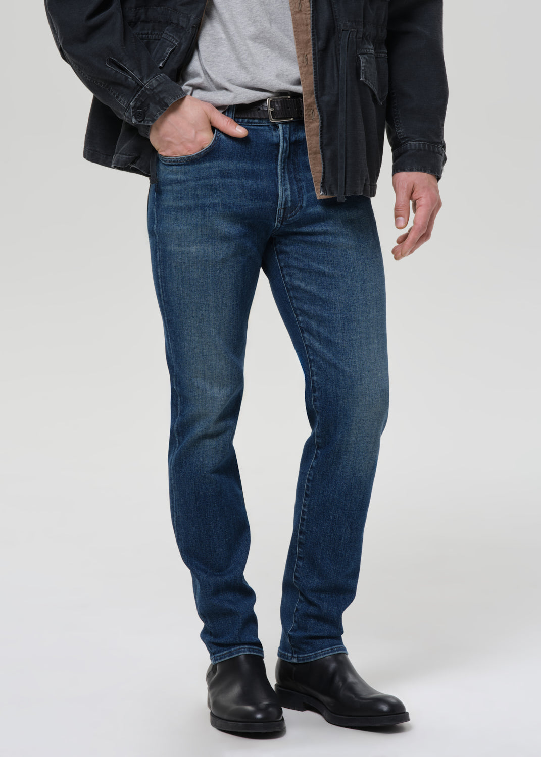 Person wearing blue jeans and a dark jacket on a grey background