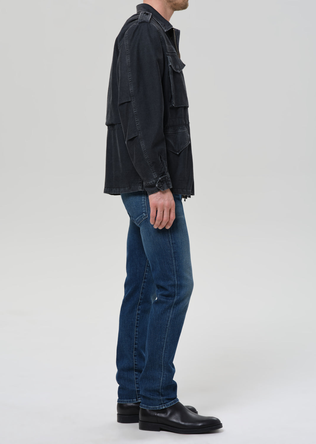 Person wearing a black jacket and blue jeans on a grey background
