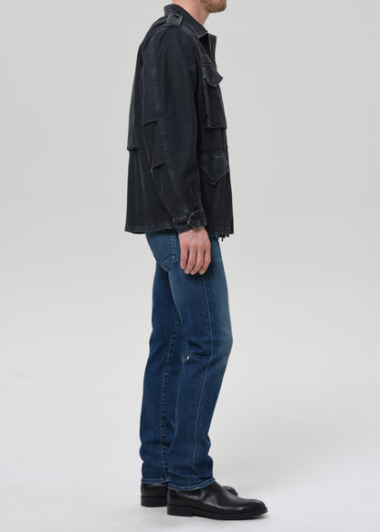 Person wearing a black jacket and blue jeans on a grey background
