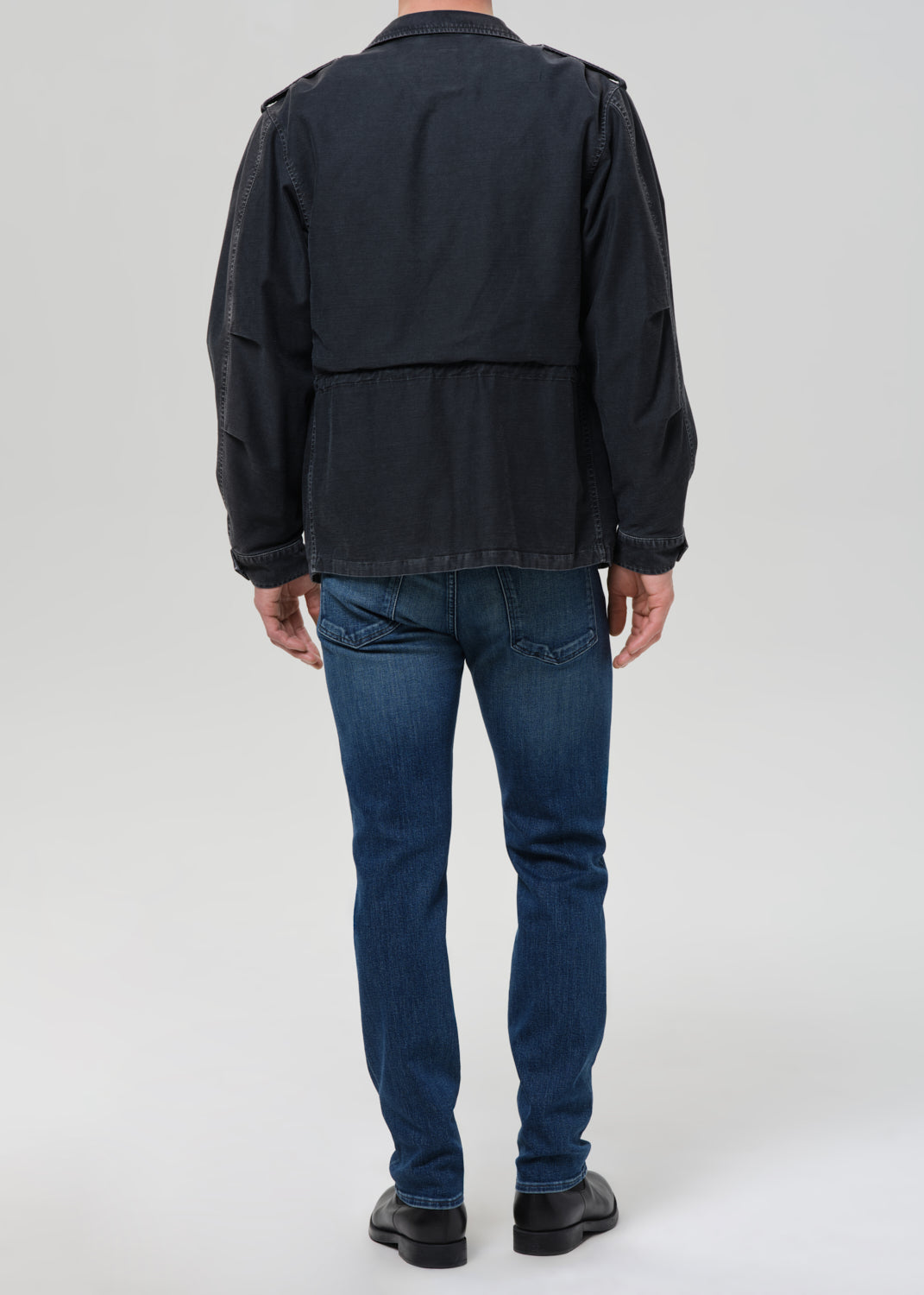 Person wearing a black jacket and blue jeans on a grey background