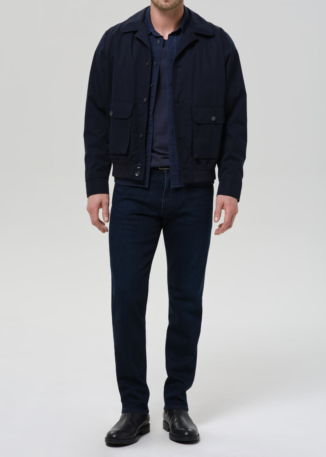 Man wearing a navy jacket, shirt, and pants on a grey background