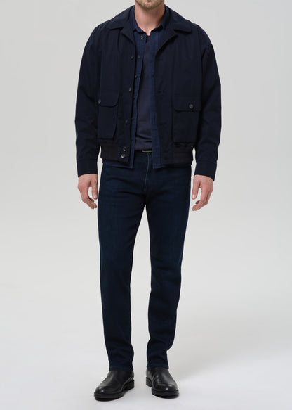 Man wearing a navy jacket, shirt, and pants on a grey background