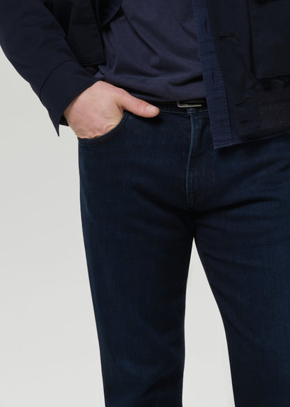 Person wearing a navy jacket and dark blue jeans on a grey background