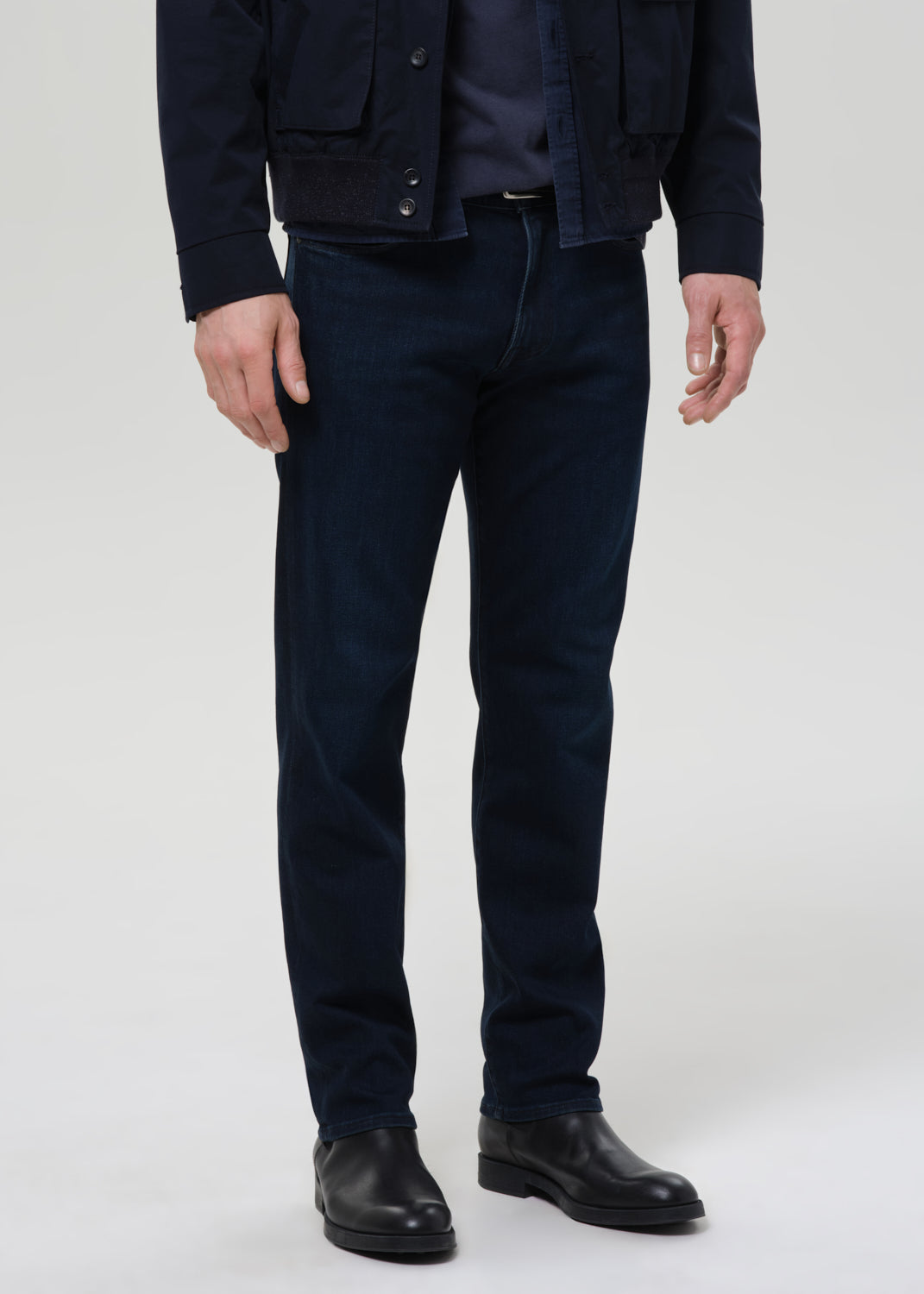 Person wearing dark blue jeans and black shoes on a grey background