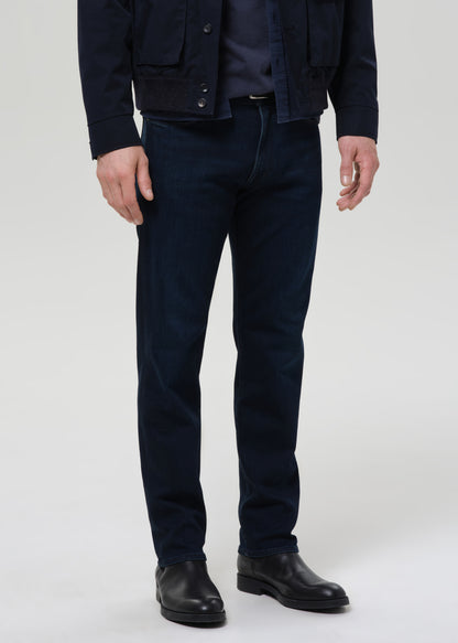 Person wearing dark blue jeans and black shoes on a grey background
