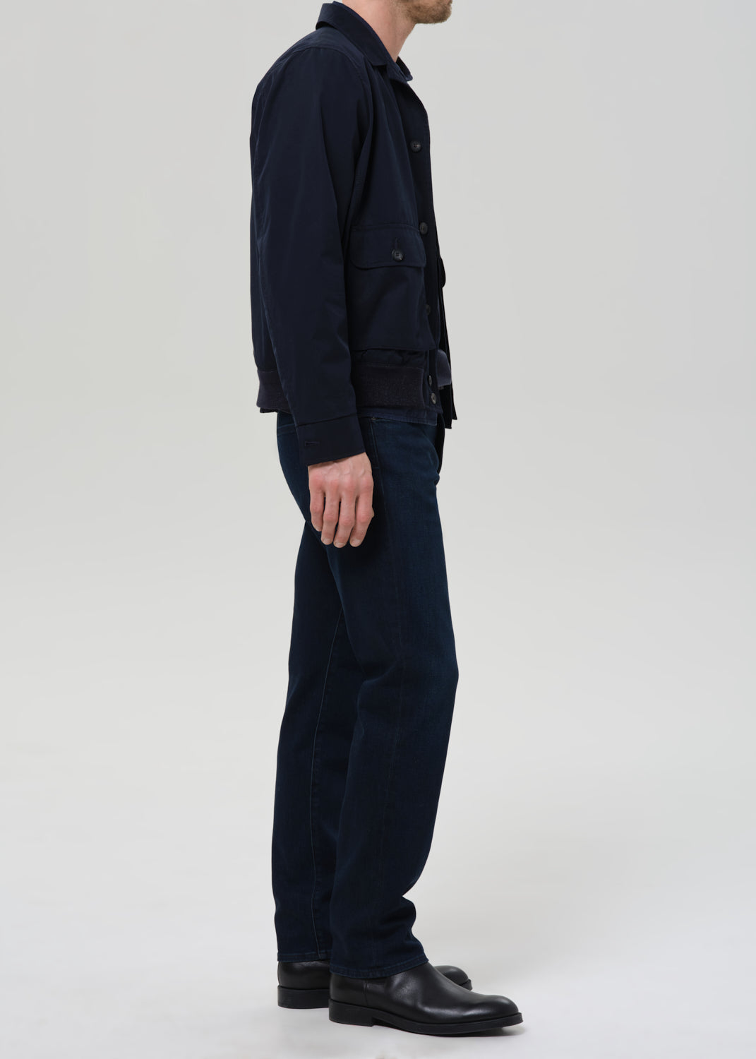 Person wearing a dark jacket, pants, and shoes on a grey background
