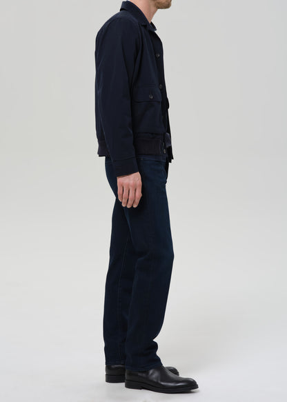 Person wearing a dark jacket, pants, and shoes on a grey background