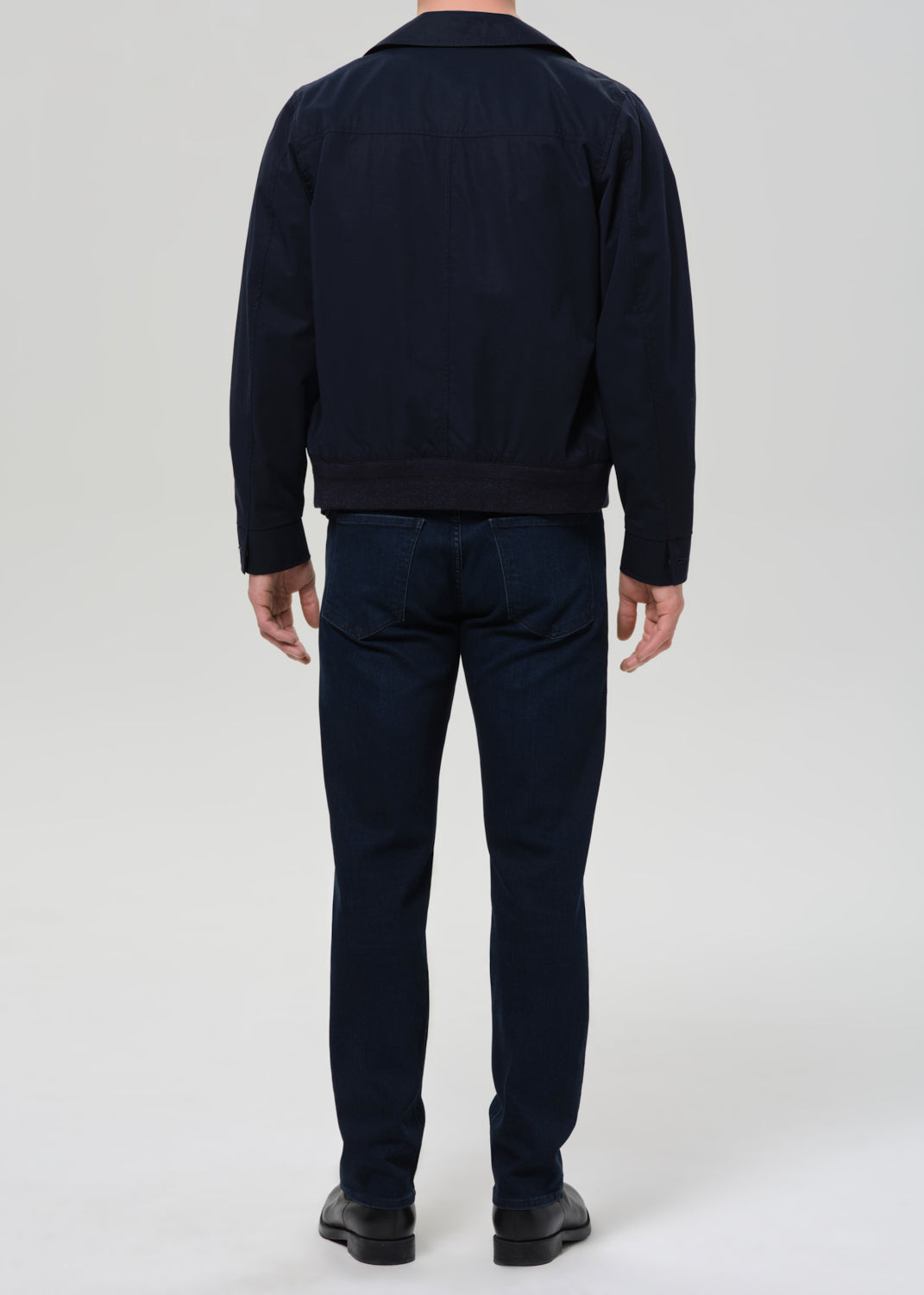 Person wearing a navy jacket and pants on a grey background