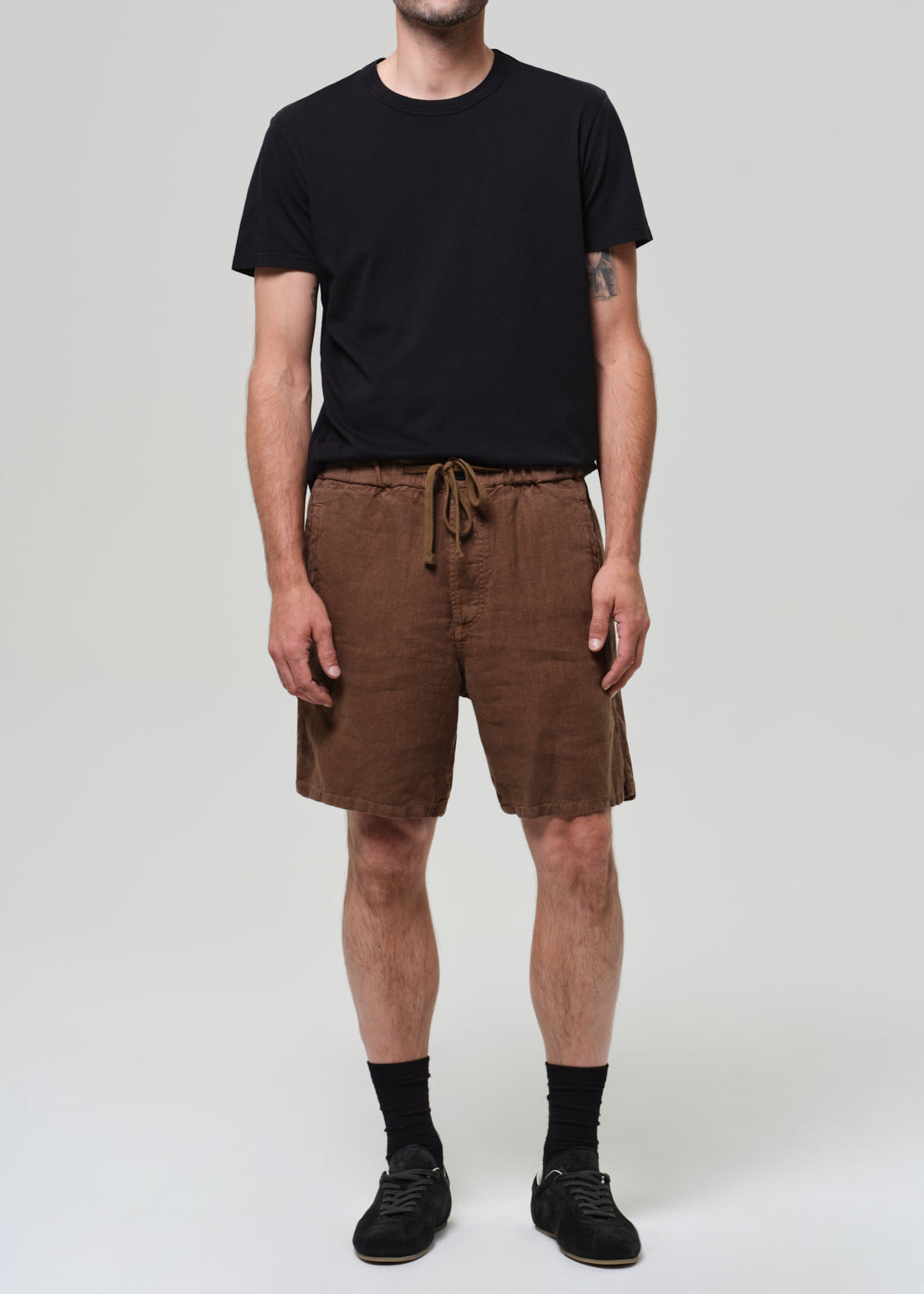 Person wearing a black t-shirt and brown shorts on a plain background