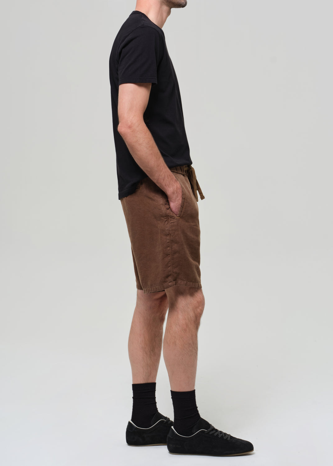 Person wearing a black t-shirt and brown shorts on a grey background