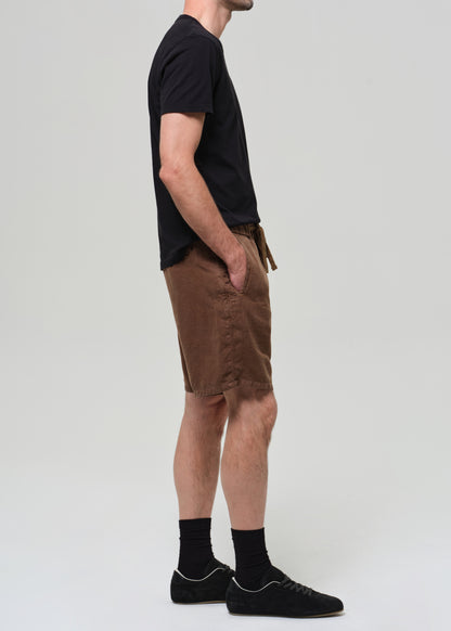 Person wearing a black t-shirt and brown shorts on a grey background