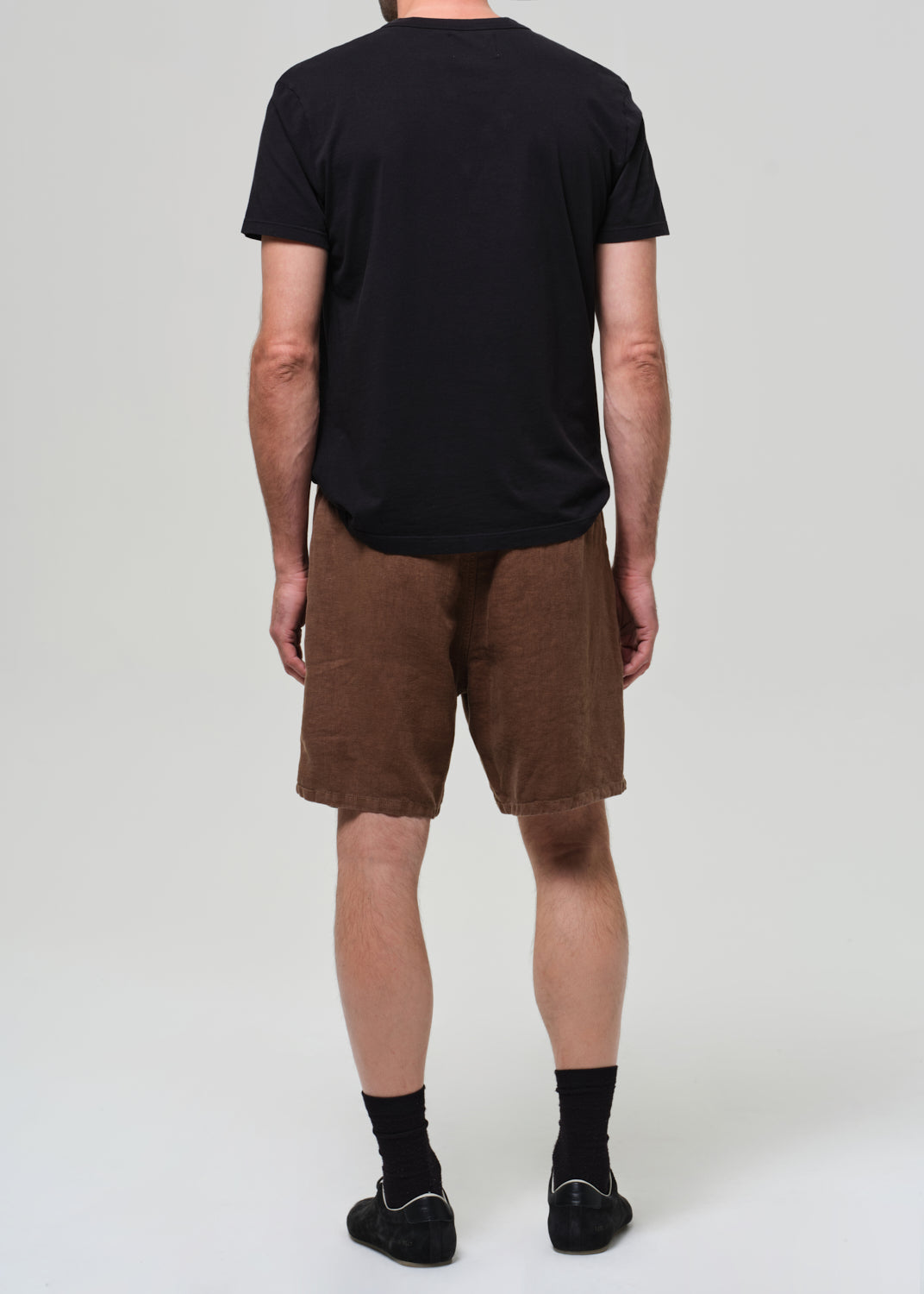Person wearing a black t-shirt and brown shorts on a grey background
