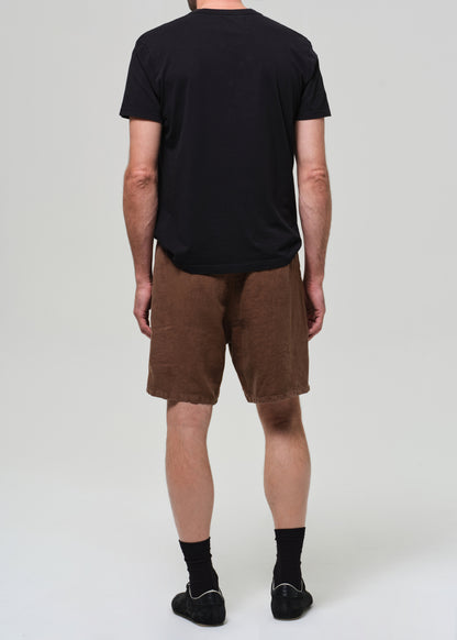 Person wearing a black t-shirt and brown shorts on a grey background