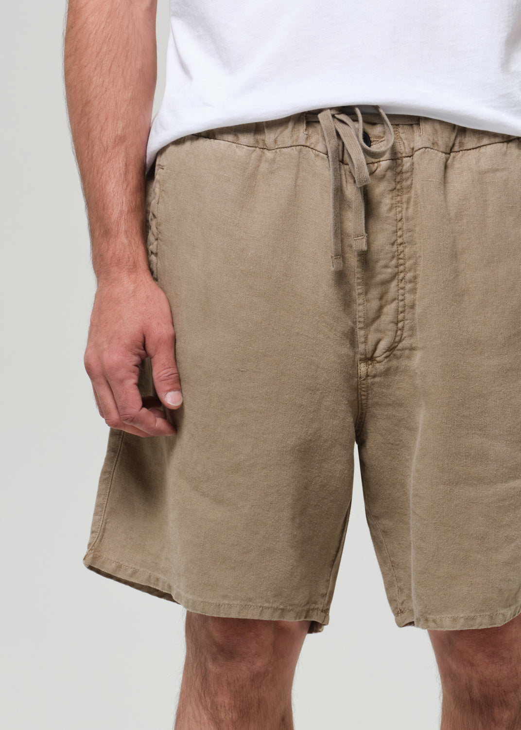 Person wearing a white t-shirt and beige linen shorts on a plain background