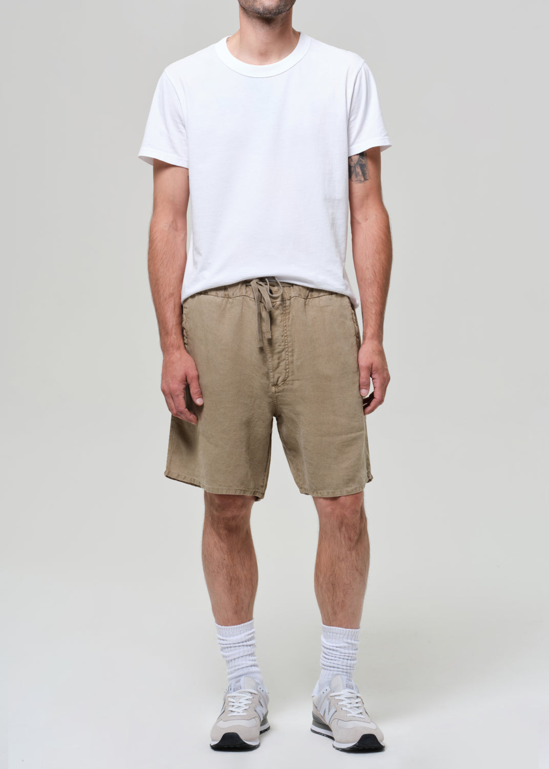 Person wearing a white t-shirt and beige linen shorts on a plain background