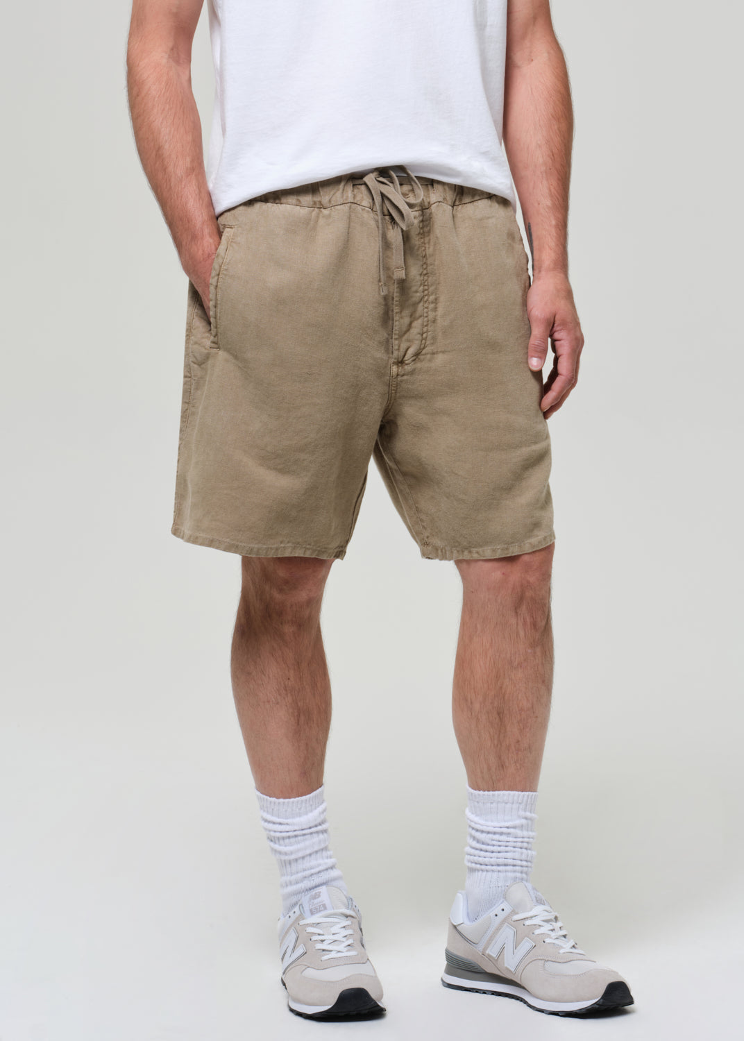 Person wearing a white t-shirt and beige linen shorts on a plain background