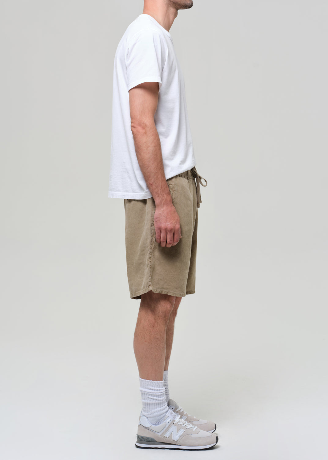 Person wearing a white t-shirt and beige linen shorts on a plain background
