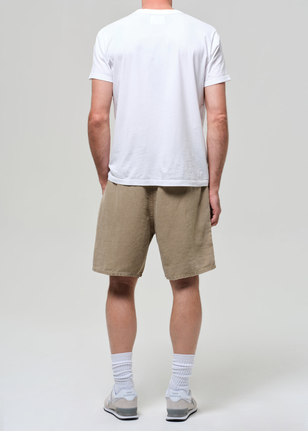 Person wearing a white t-shirt and beige linen shorts on a plain background