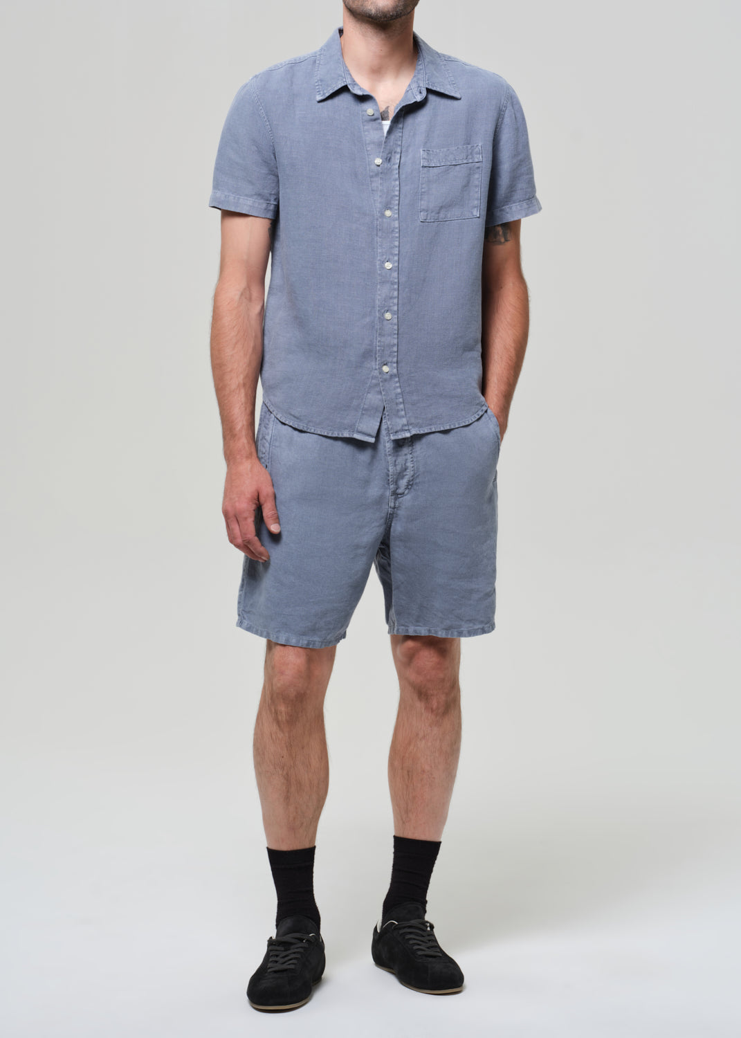 Man wearing a blue button-up shirt and shorts on a plain background