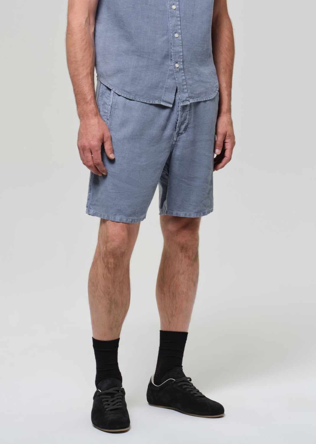 Man wearing a blue button-up shirt and shorts on a plain background