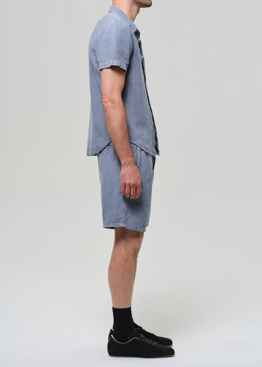 Man wearing a blue button-up shirt and shorts on a plain background