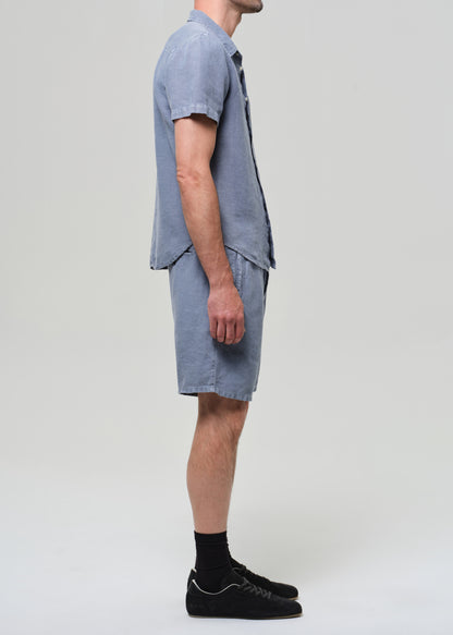 Man wearing a blue button-up shirt and shorts on a plain background