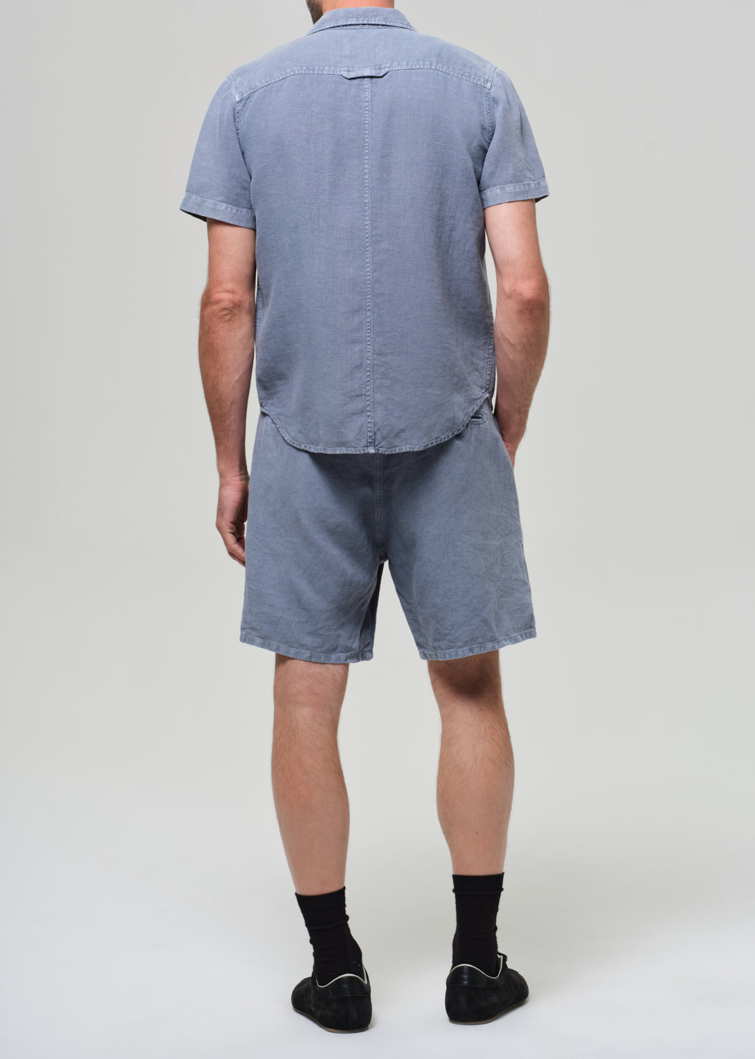 Man wearing a blue button-up shirt and shorts on a plain background