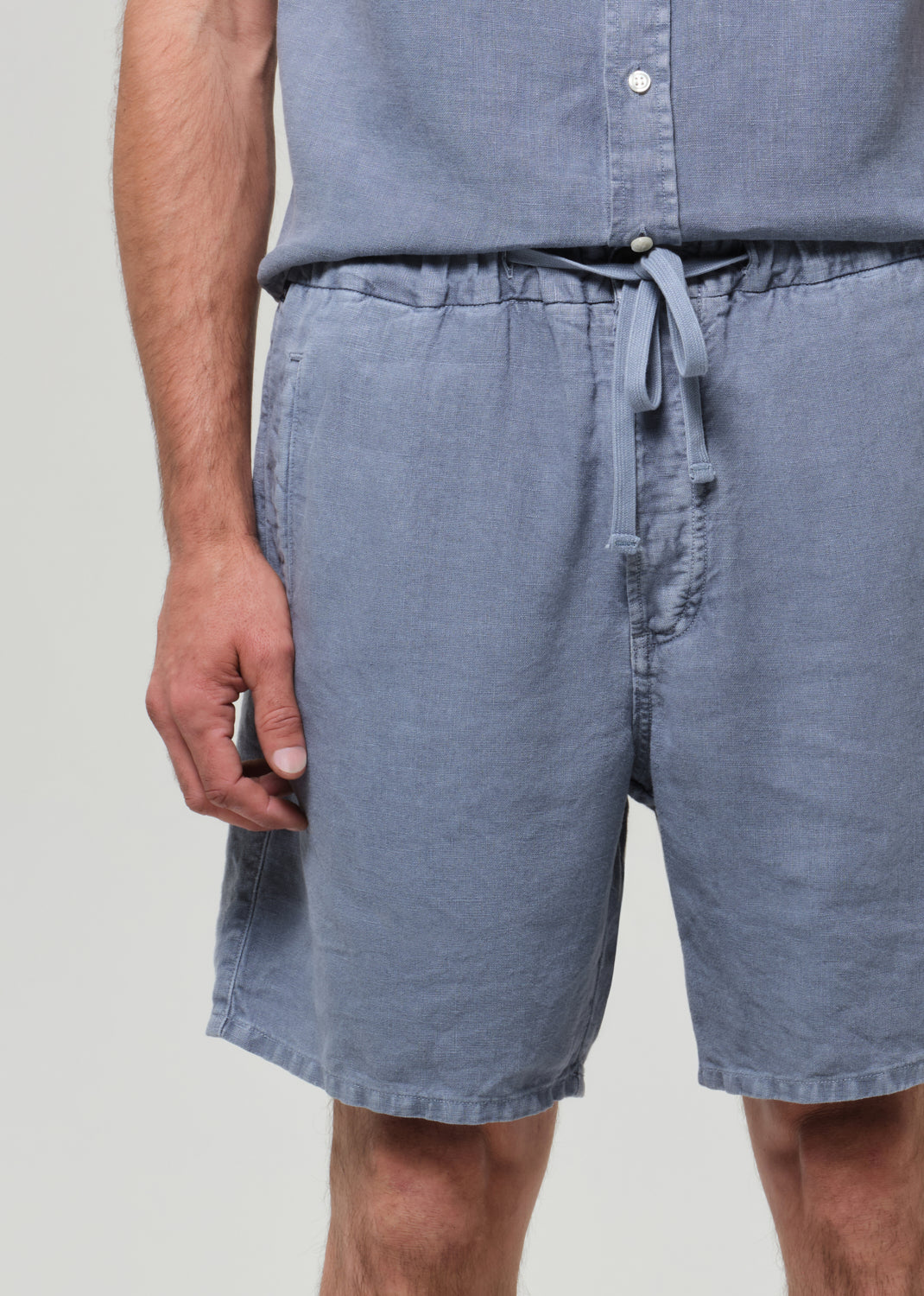 Man wearing a blue button-up shirt and shorts on a plain background