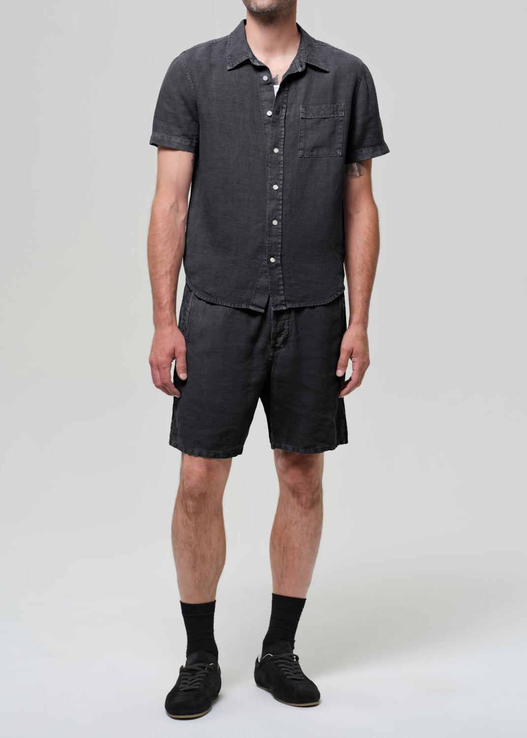 Person wearing a washed black button-up shirt and shorts on a plain background