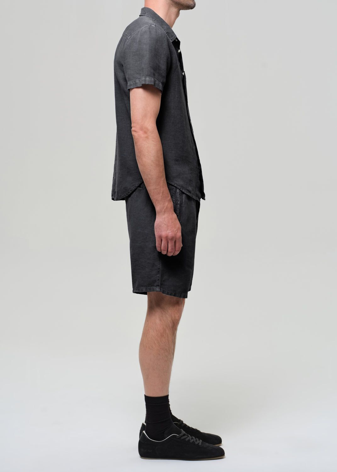 Person wearing a washed black button-up shirt and shorts on a plain background