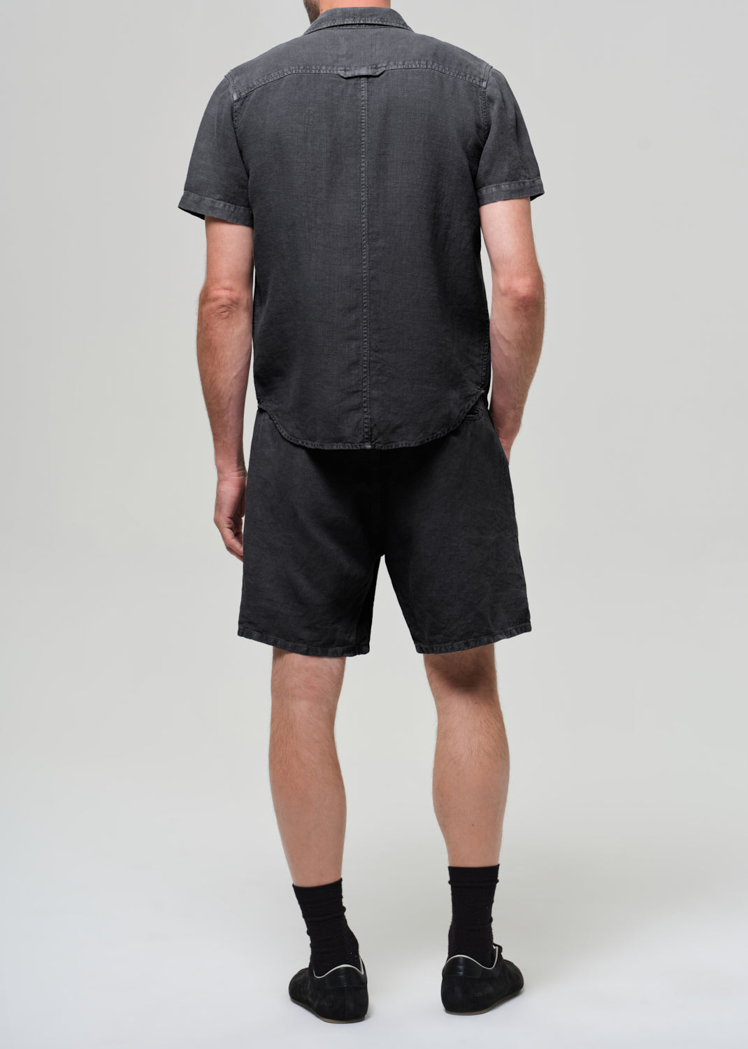 Person wearing a washed black button-up shirt and shorts on a plain background
