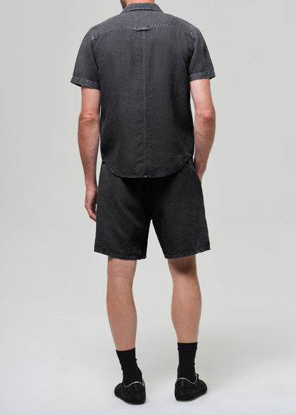 Person wearing a washed black button-up shirt and shorts on a plain background