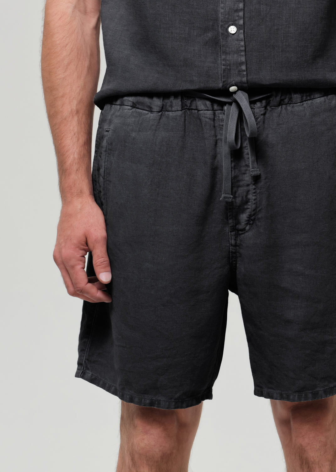 Person wearing a washed black button-up shirt and shorts on a plain background