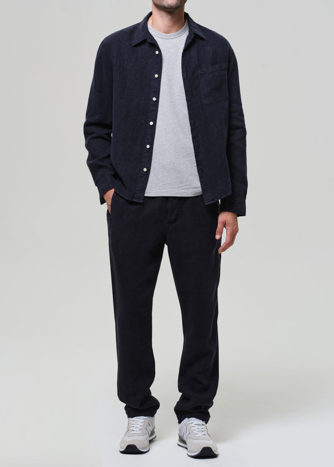 Person wearing a navy linen button-up shirt, gray t-shirt, navy linen pants, and sneakers on a light gray background