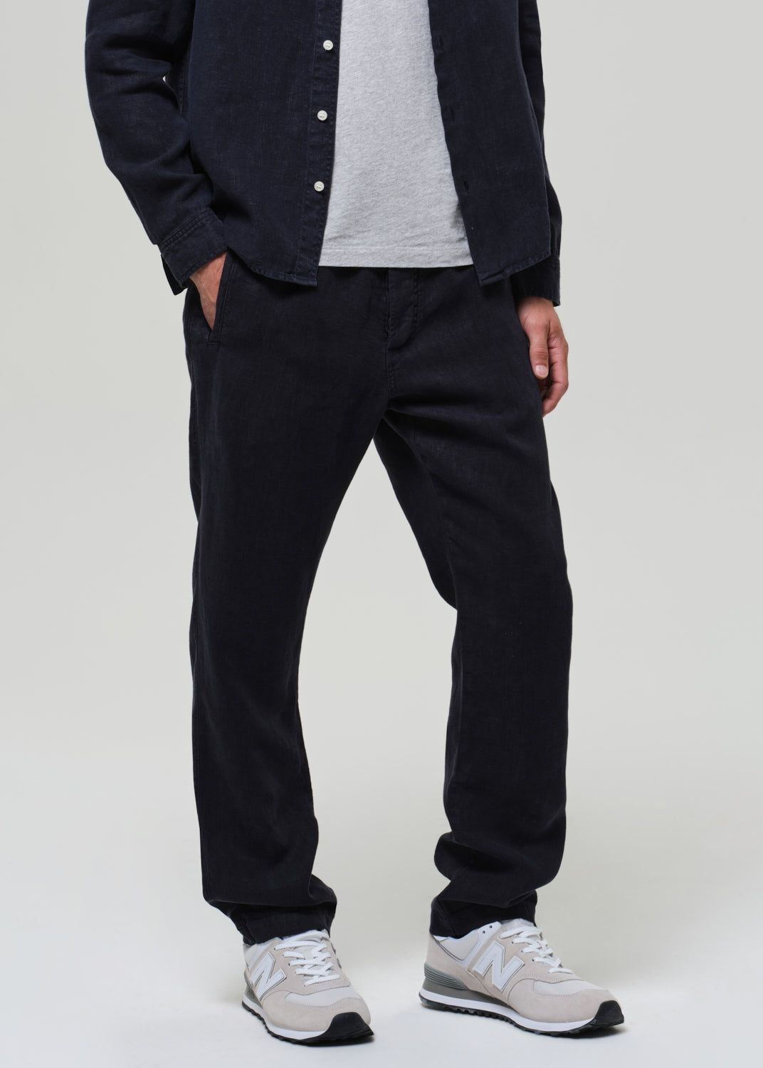 Person wearing a navy linen button-up shirt, gray t-shirt, navy linen pants, and sneakers on a light gray background