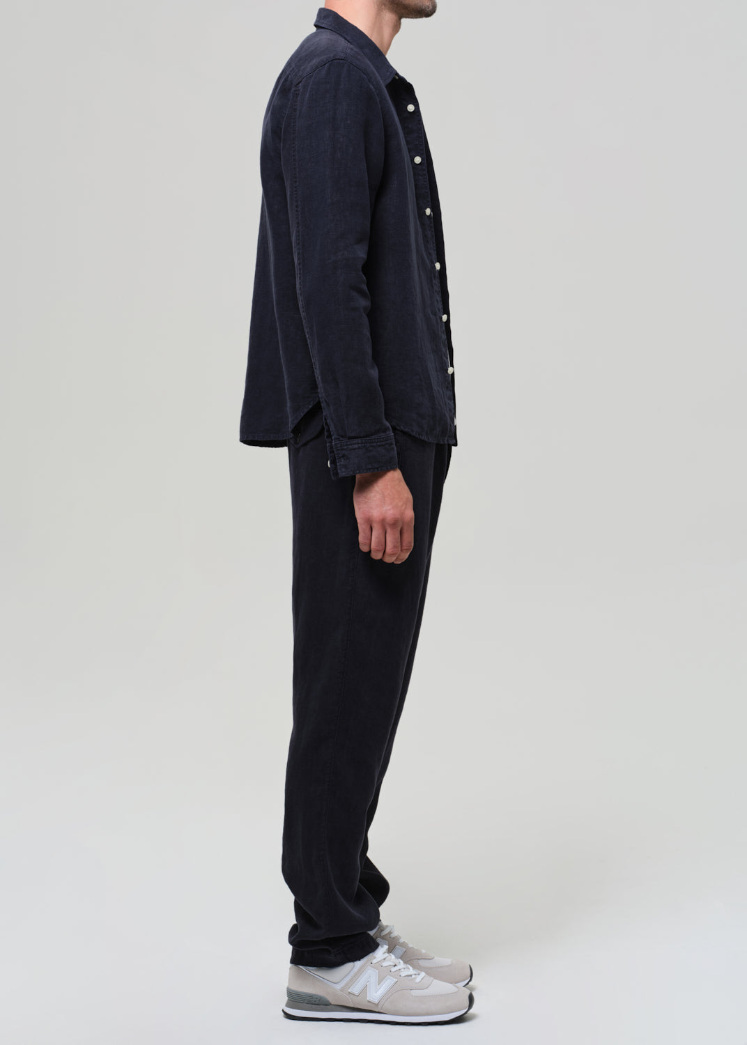 Person wearing a navy linen button-up shirt, gray t-shirt, navy linen pants, and sneakers on a light gray background