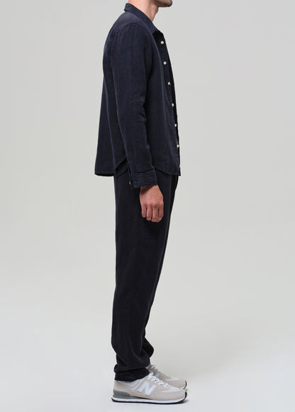 Person wearing a navy linen button-up shirt, gray t-shirt, navy linen pants, and sneakers on a light gray background