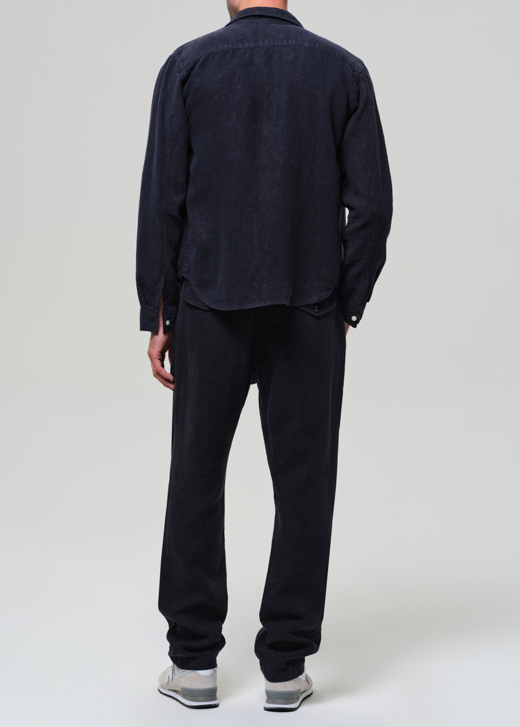 Person wearing a navy linen button-up shirt, gray t-shirt, navy linen pants, and sneakers on a light gray background