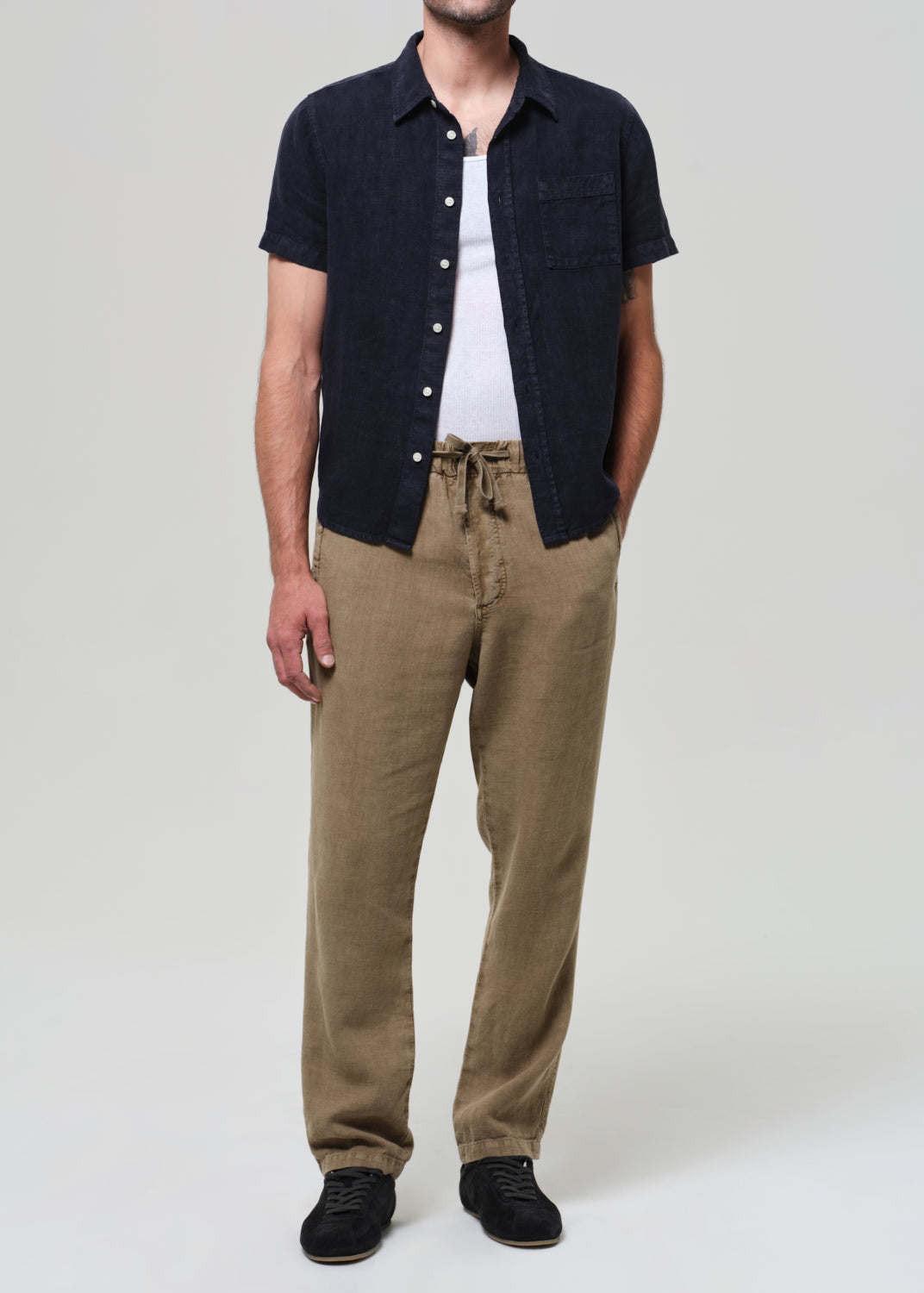 Person wearing a black short-sleeve shirt, white t-shirt, and beige pants on a plain background