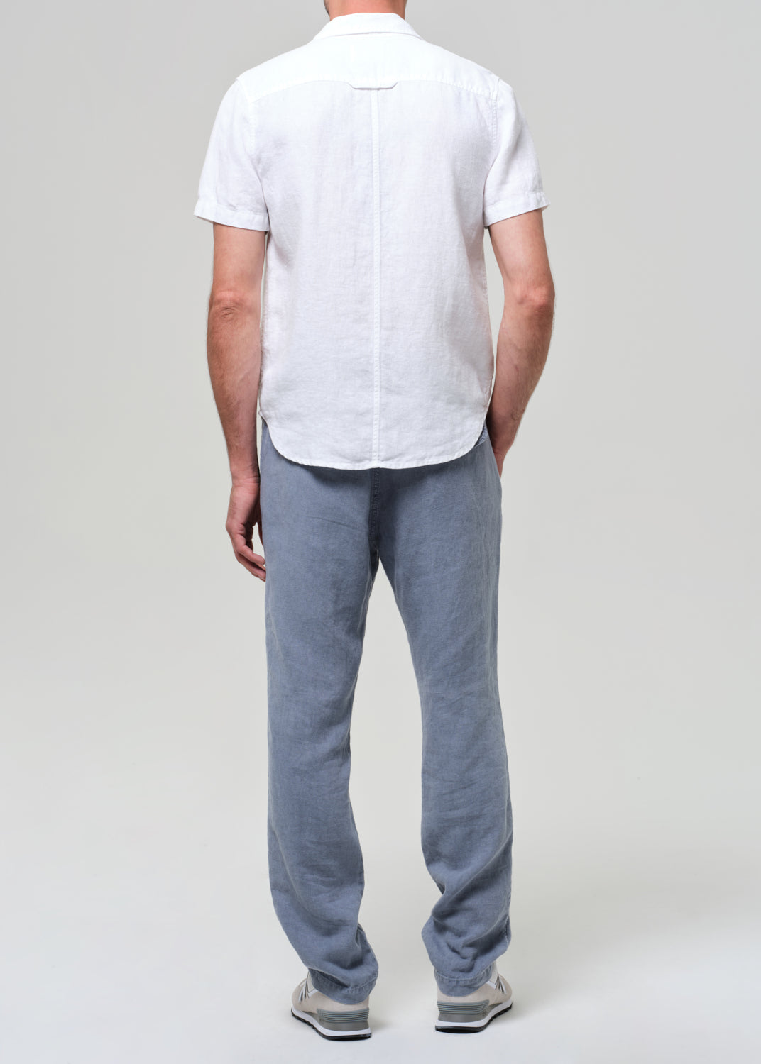 Person wearing a white short-sleeve shirt and light blue pants on a plain background