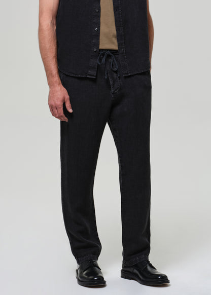 Person wearing a black short-sleeve linen shirt over a beige t-shirt, paired with black linen pants on a grey background