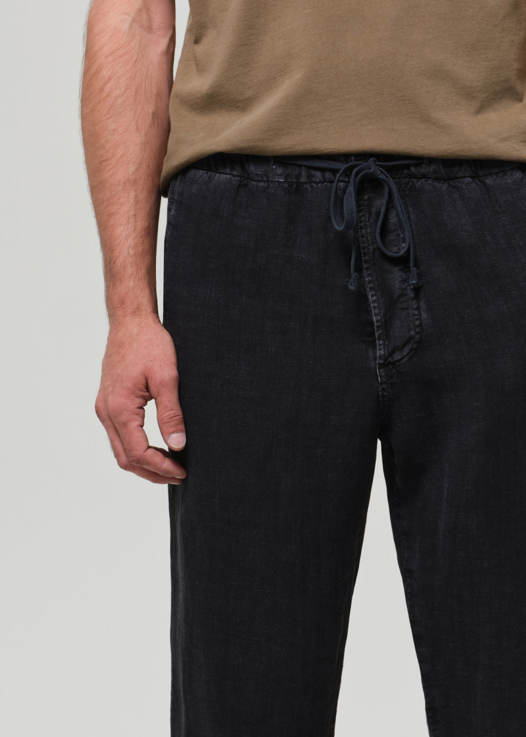 Person wearing black pants with a drawstring and a brown top on a light gray background