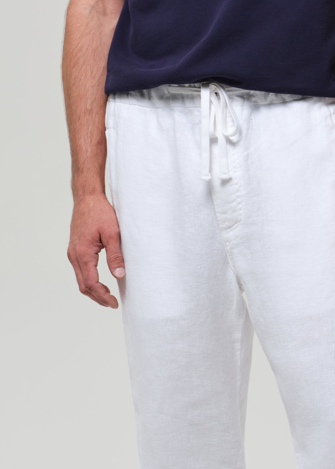 Person wearing a navy polo shirt and white linen pants on a plain background