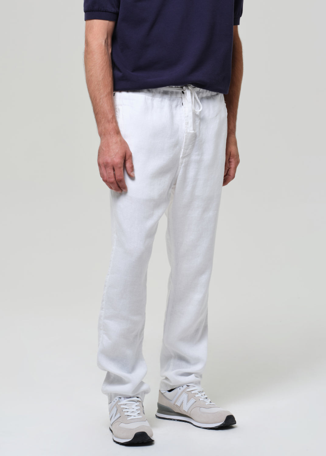 Person wearing a navy polo shirt and white linen pants on a plain background