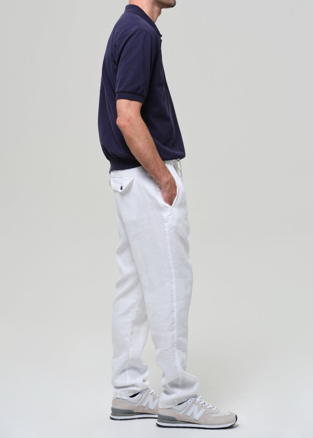 Person wearing a navy polo shirt and white linen pants on a plain background