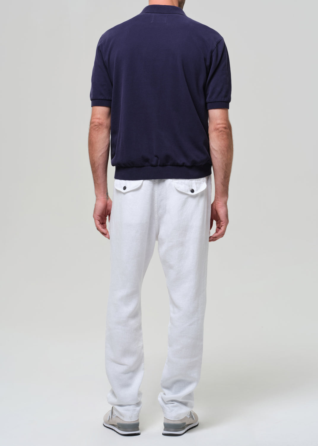 Person wearing a navy polo shirt and white linen pants on a plain background