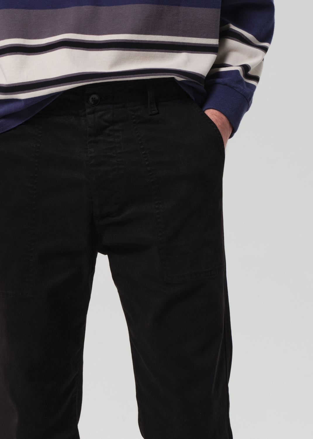 Person wearing black pants and a striped sweater on a plain background