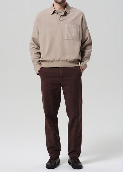 Person wearing a beige sweater and brown pants on a plain background